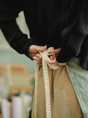 Back view crop anonymous female cafeteria or store worker tying up apron lace straps before duty